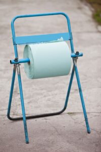Blue metal stand holding a roll of light green centre feed paper for dispensing.