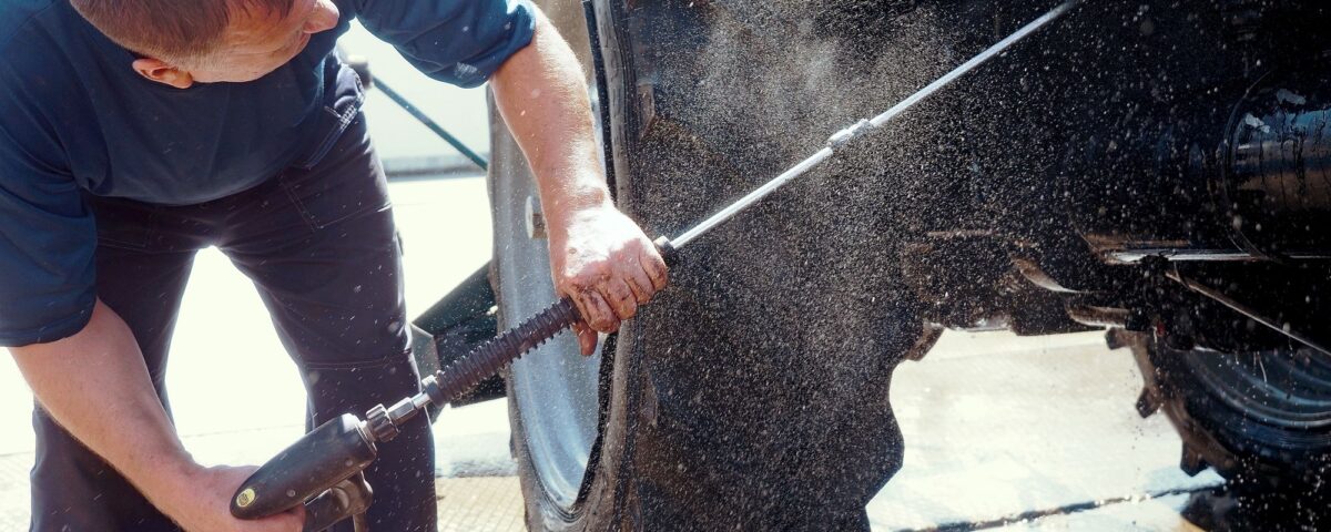 Individual operating a pressure washer to clean the wheels and body of a tractor.