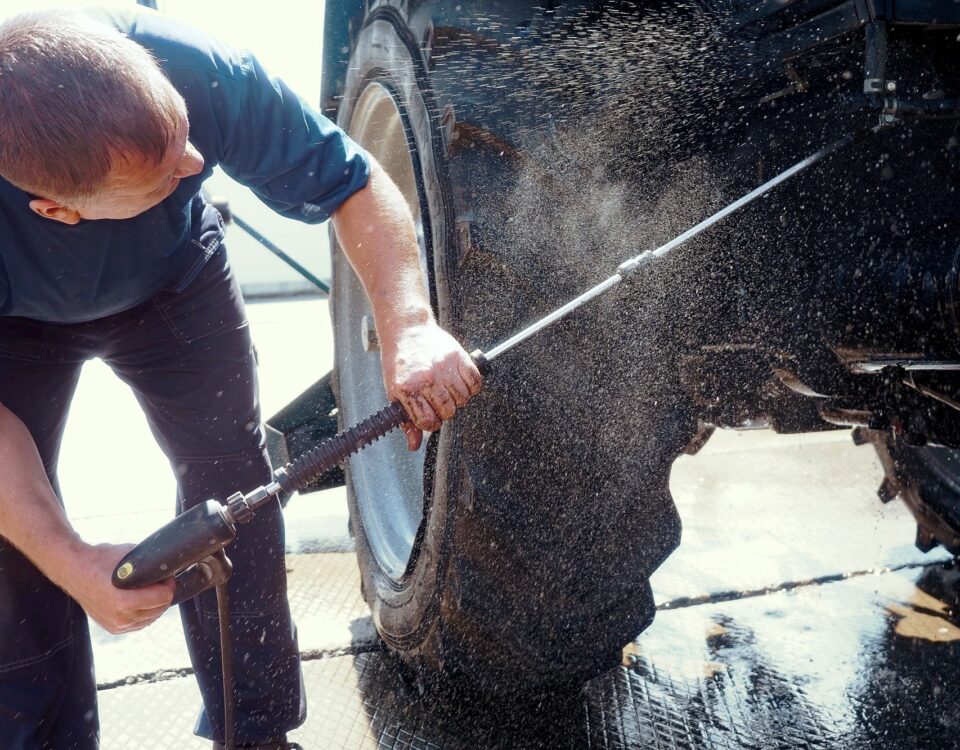 Individual operating a pressure washer to clean the wheels and body of a tractor.