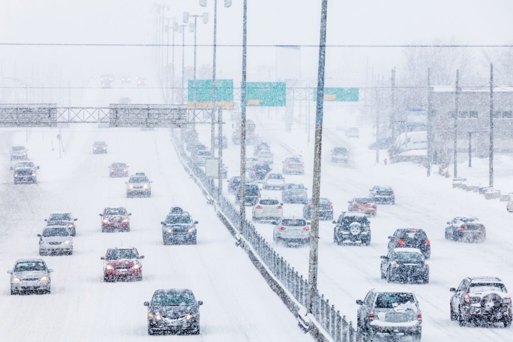 Vehicles navigating a snowy highway during a winter storm with reduced visibility and heavy snowfall.