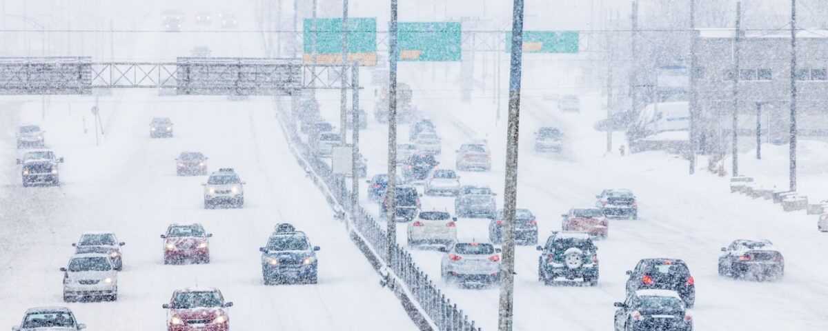 Vehicles navigating a snowy highway during a winter storm with reduced visibility and heavy snowfall.