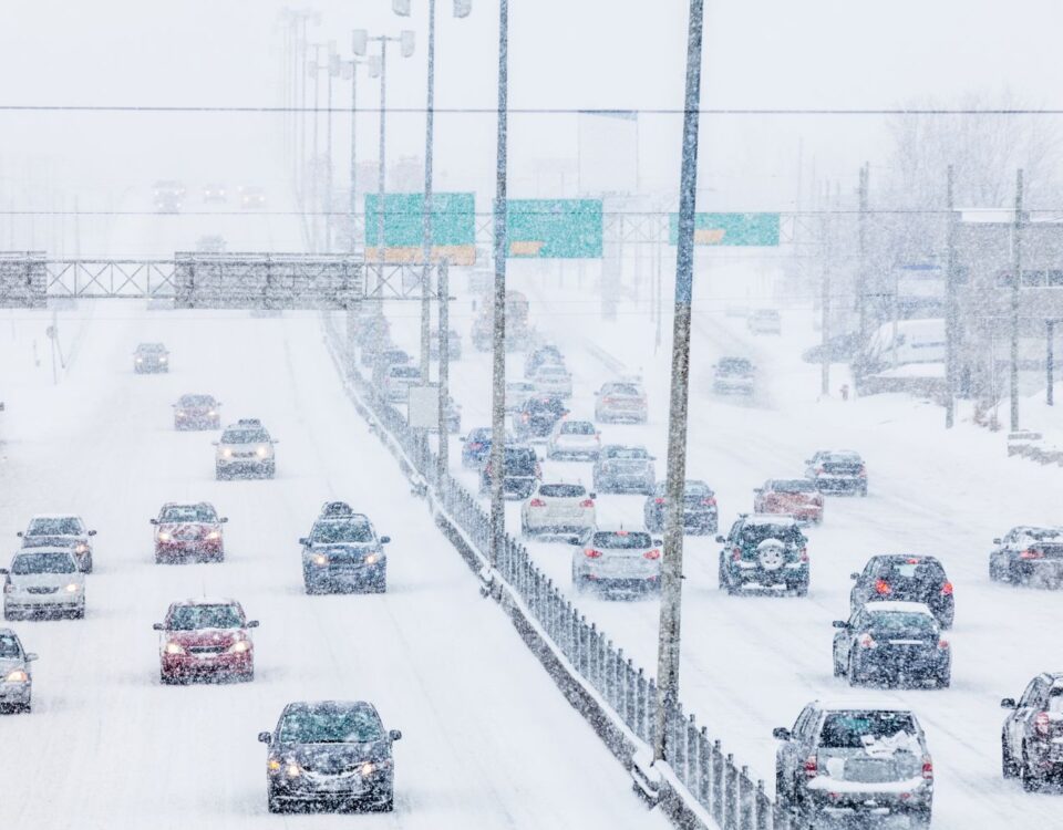 Vehicles navigating a snowy highway during a winter storm with reduced visibility and heavy snowfall.